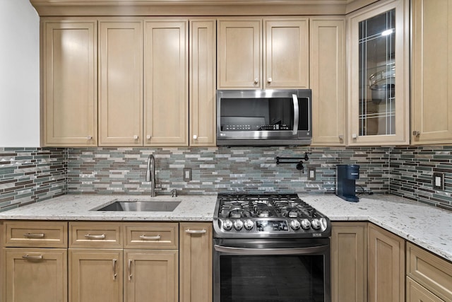 kitchen with tasteful backsplash, glass insert cabinets, light stone countertops, stainless steel appliances, and a sink