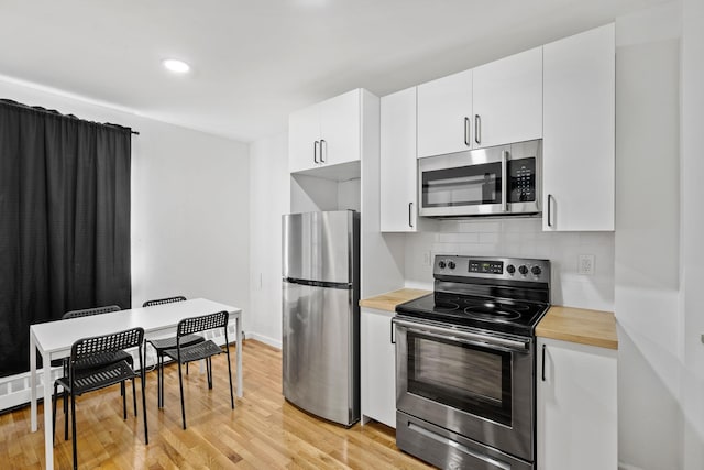 kitchen with light wood-style flooring, stainless steel appliances, butcher block counters, white cabinets, and backsplash