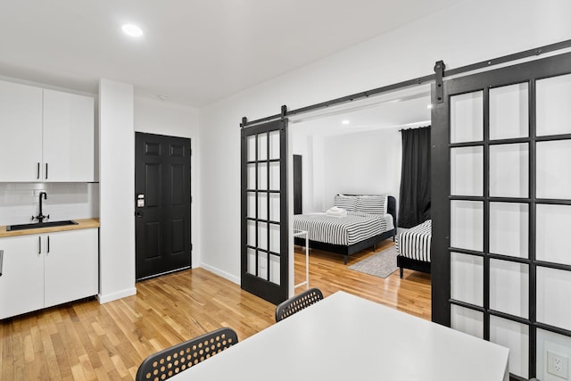 bedroom featuring a barn door, a sink, light wood-style flooring, and recessed lighting