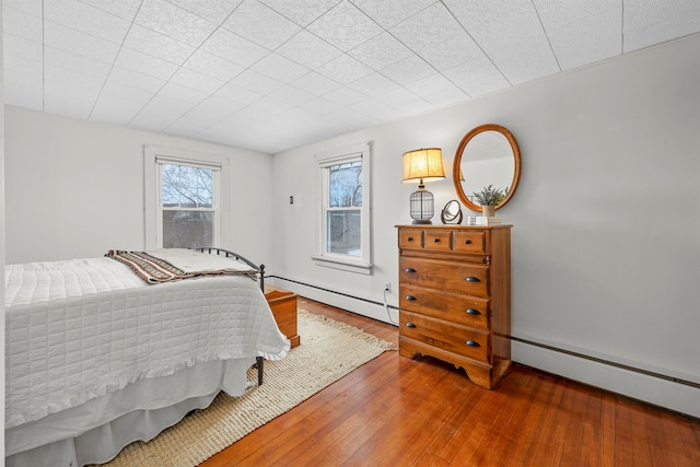 bedroom with a baseboard heating unit, wood-type flooring, and multiple windows