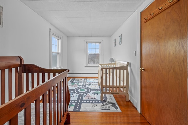 bedroom featuring a nursery area, a baseboard radiator, and wood finished floors