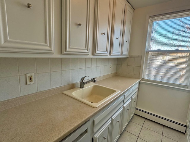 kitchen with tasteful backsplash, light countertops, baseboard heating, light tile patterned flooring, and a sink