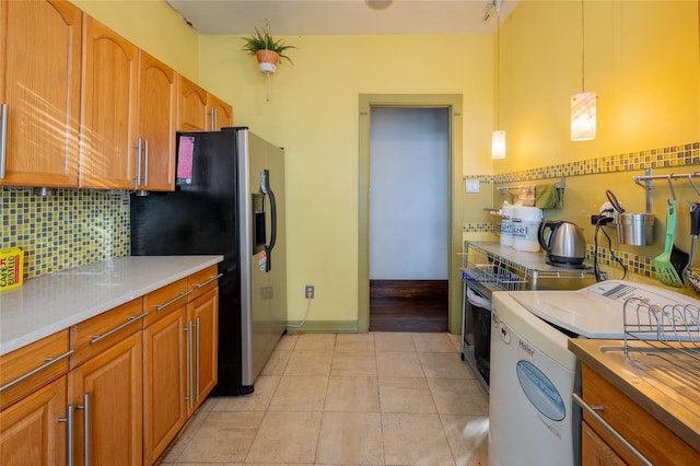 kitchen with stainless steel refrigerator with ice dispenser, tasteful backsplash, washer / clothes dryer, light countertops, and hanging light fixtures