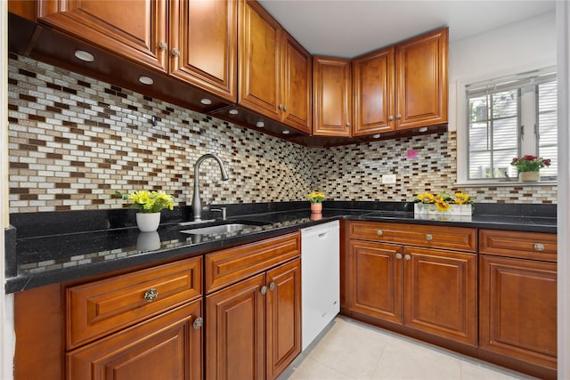 kitchen featuring decorative backsplash, brown cabinetry, white dishwasher, a sink, and dark stone counters