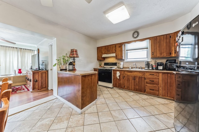 kitchen with brown cabinets, white range with gas stovetop, light countertops, and under cabinet range hood