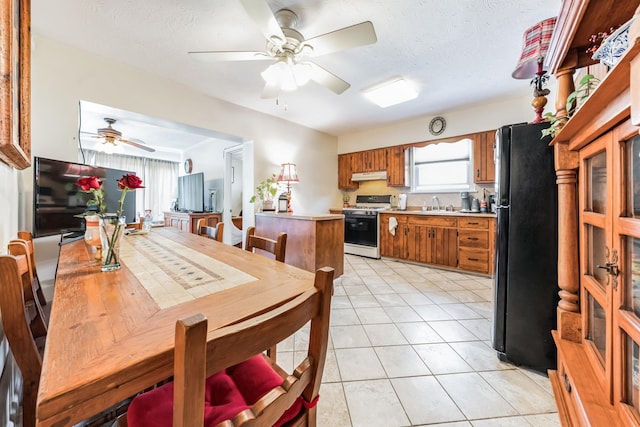 kitchen featuring brown cabinetry, freestanding refrigerator, white gas stove, under cabinet range hood, and light tile patterned flooring