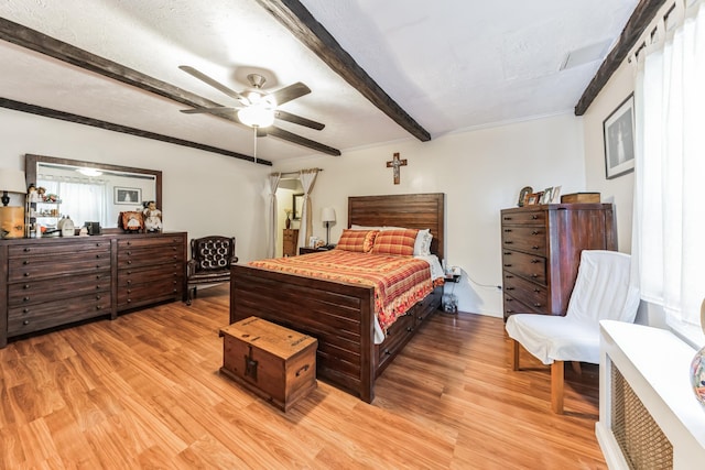 bedroom featuring a textured ceiling, light wood finished floors, beam ceiling, and a ceiling fan