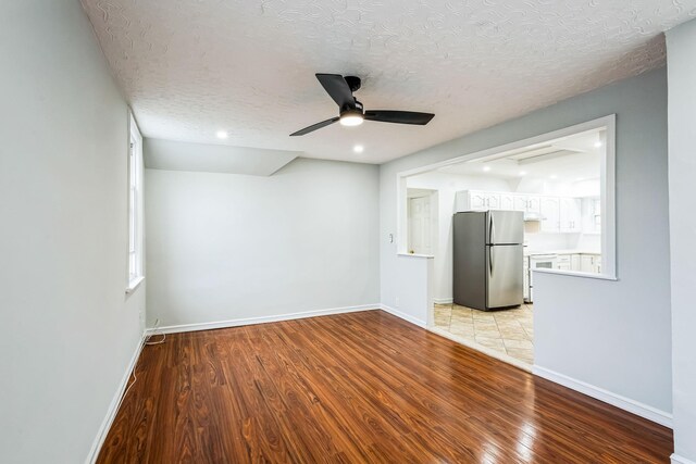 empty room with a textured ceiling, ceiling fan, light wood-type flooring, and baseboards