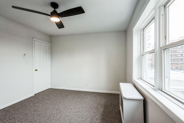 empty room with dark colored carpet, a ceiling fan, and baseboards