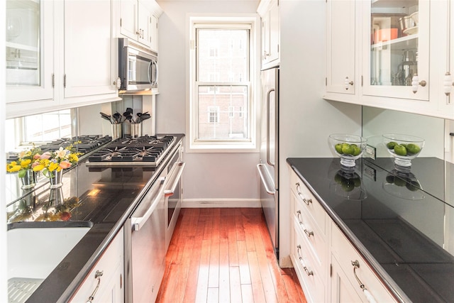 kitchen featuring stainless steel appliances, glass insert cabinets, light wood-style flooring, and white cabinets