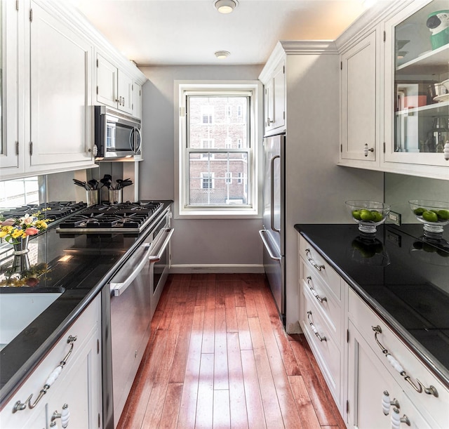 kitchen with appliances with stainless steel finishes, glass insert cabinets, hardwood / wood-style flooring, and white cabinetry