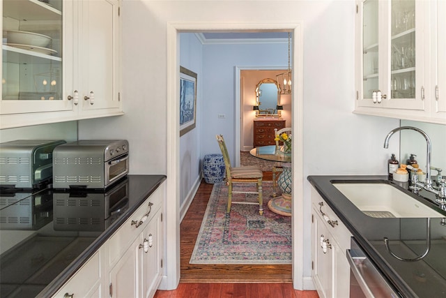 kitchen with dark wood-style flooring, dark countertops, white cabinets, a sink, and dishwasher