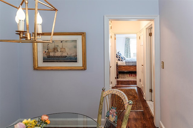 corridor featuring baseboards, wood finished floors, and an inviting chandelier