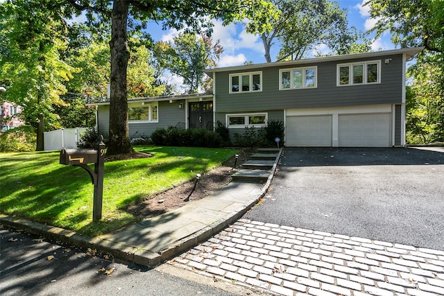 tri-level home featuring driveway, an attached garage, fence, and a front yard