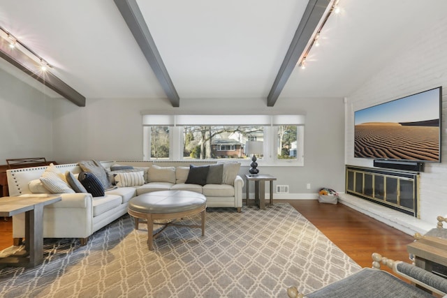 living area with rail lighting, lofted ceiling with beams, a glass covered fireplace, wood finished floors, and baseboards