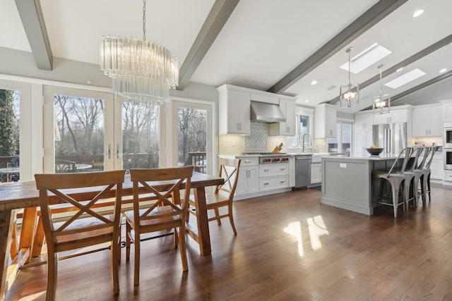 dining area featuring french doors, lofted ceiling with skylight, dark wood finished floors, and an inviting chandelier