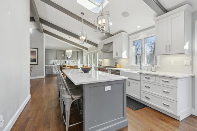 kitchen with a breakfast bar, a center island, white cabinetry, a sink, and wall chimney range hood