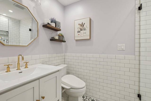 bathroom featuring a wainscoted wall, tile walls, visible vents, toilet, and vanity