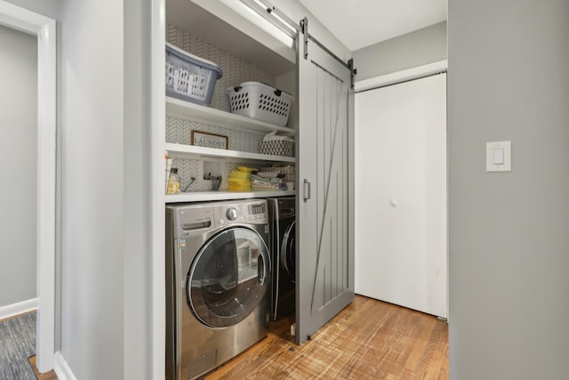 washroom featuring laundry area, washing machine and clothes dryer, light wood finished floors, and a barn door