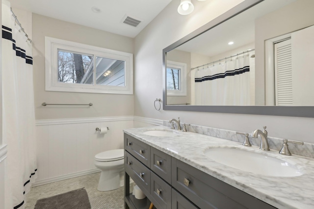 bathroom with a closet, a wainscoted wall, a sink, and double vanity