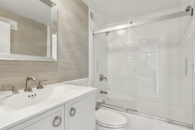 bathroom featuring toilet, bath / shower combo with glass door, tile walls, and vanity