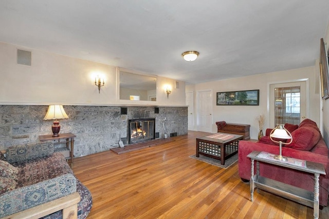 living room with a stone fireplace, wood finished floors, and visible vents