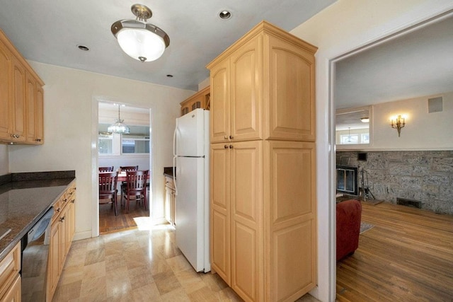 kitchen featuring light brown cabinets, stainless steel dishwasher, freestanding refrigerator, dark stone counters, and a stone fireplace