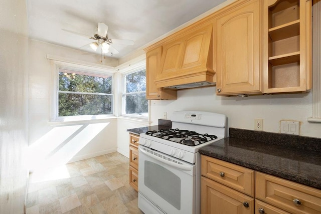 kitchen featuring a ceiling fan, dark stone counters, white range with gas stovetop, and light brown cabinets