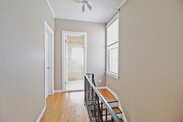 corridor featuring light wood-style flooring, baseboards, crown molding, and an upstairs landing