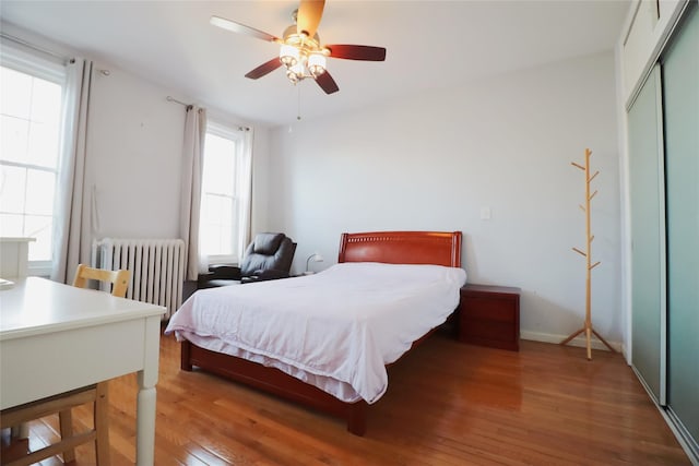 bedroom featuring a closet, ceiling fan, radiator heating unit, and wood finished floors