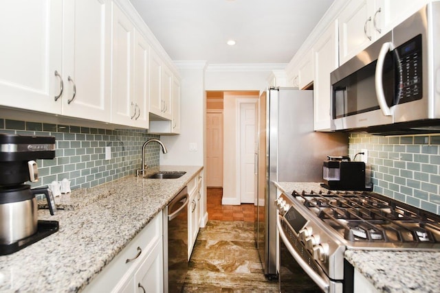 kitchen featuring white cabinets, appliances with stainless steel finishes, ornamental molding, light stone countertops, and a sink