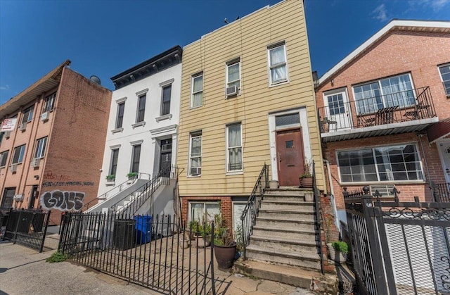 multi unit property featuring stairs, brick siding, a fenced front yard, and cooling unit