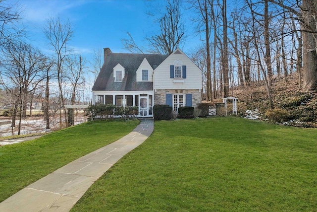 cape cod house with stone siding, a chimney, and a front yard