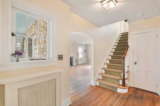 entrance foyer featuring arched walkways, a fireplace with flush hearth, baseboards, stairs, and wood-type flooring