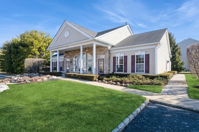 neoclassical home featuring stone siding, a shingled roof, and a front yard