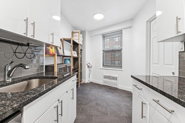 kitchen with backsplash, radiator heating unit, white cabinetry, a sink, and dark stone counters