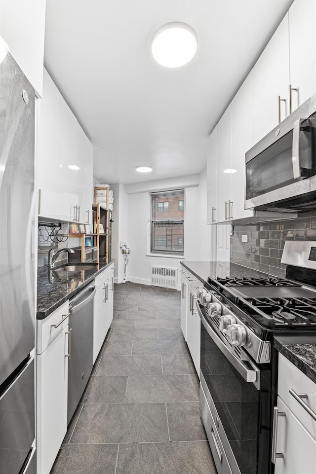 kitchen with stainless steel appliances, a sink, white cabinetry, decorative backsplash, and radiator