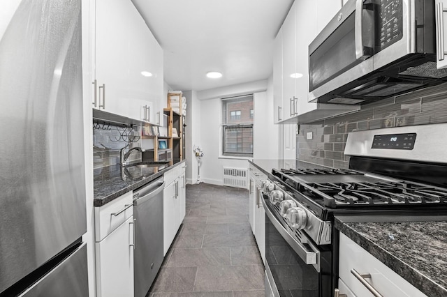 kitchen featuring stainless steel appliances, a sink, white cabinetry, backsplash, and radiator heating unit