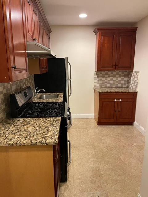 kitchen with reddish brown cabinets, baseboards, light stone counters, and gas stove