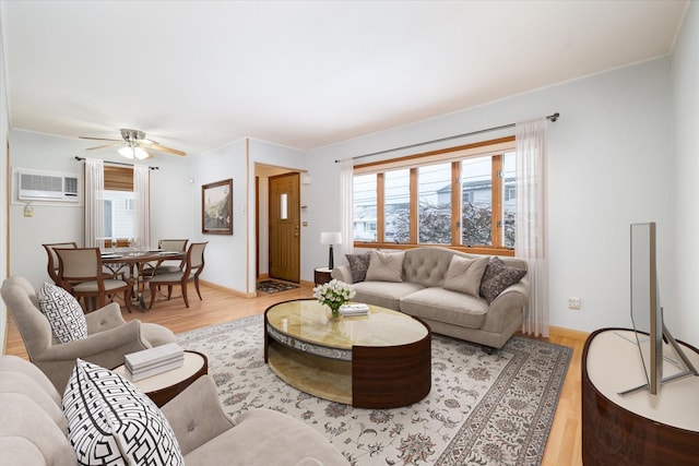 living area featuring a ceiling fan, a wall unit AC, light wood-style flooring, and baseboards