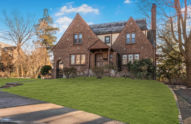 tudor home featuring brick siding, a chimney, a front lawn, and stucco siding