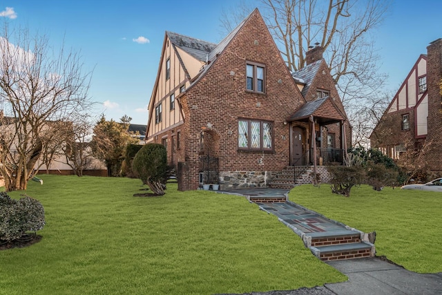 tudor home with brick siding, a chimney, and a front yard