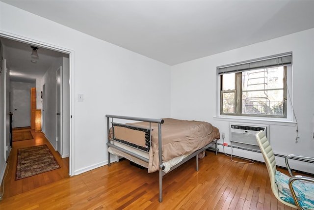 bedroom featuring baseboards, wood finished floors, and a wall mounted air conditioner