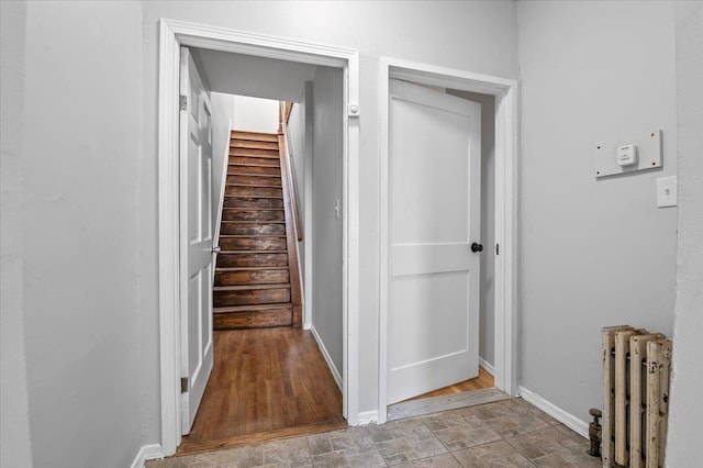 stairway featuring baseboards, stone finish floor, and radiator