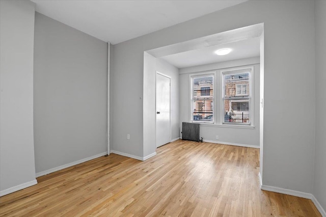 empty room with radiator, light wood finished floors, and baseboards