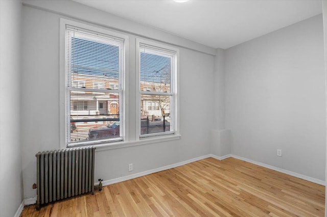 empty room featuring baseboards, light wood-style flooring, and radiator heating unit