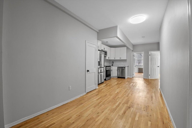 unfurnished living room featuring light wood-style flooring, baseboards, and a sink