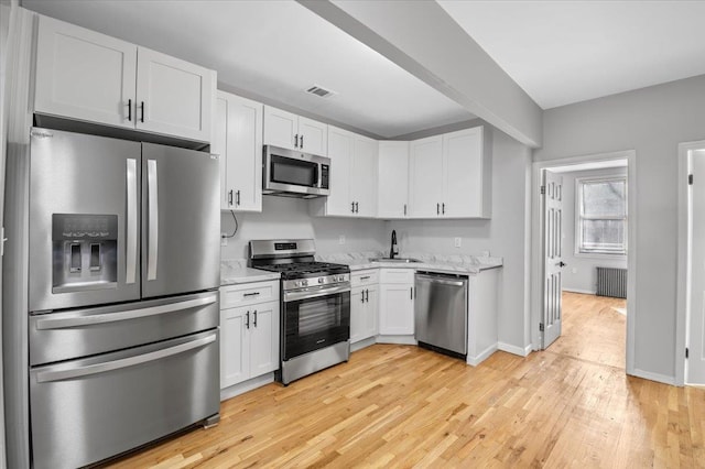 kitchen featuring light stone counters, stainless steel appliances, radiator, visible vents, and white cabinets