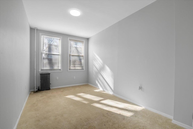 spare room with radiator, light colored carpet, and baseboards