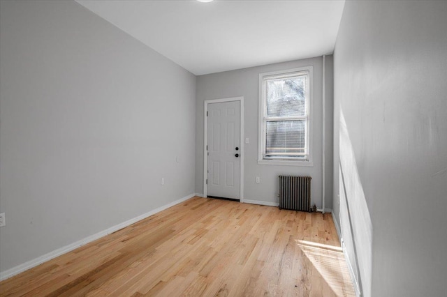 spare room with baseboards, light wood-style flooring, and radiator